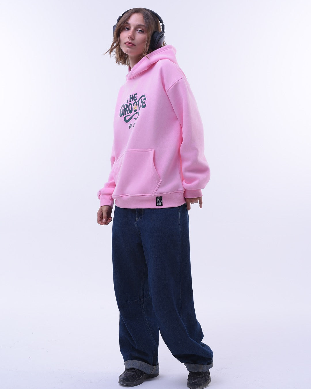 Girl wearing pink oversized hoodie for women with graphic print and dark loose jeans with headphones