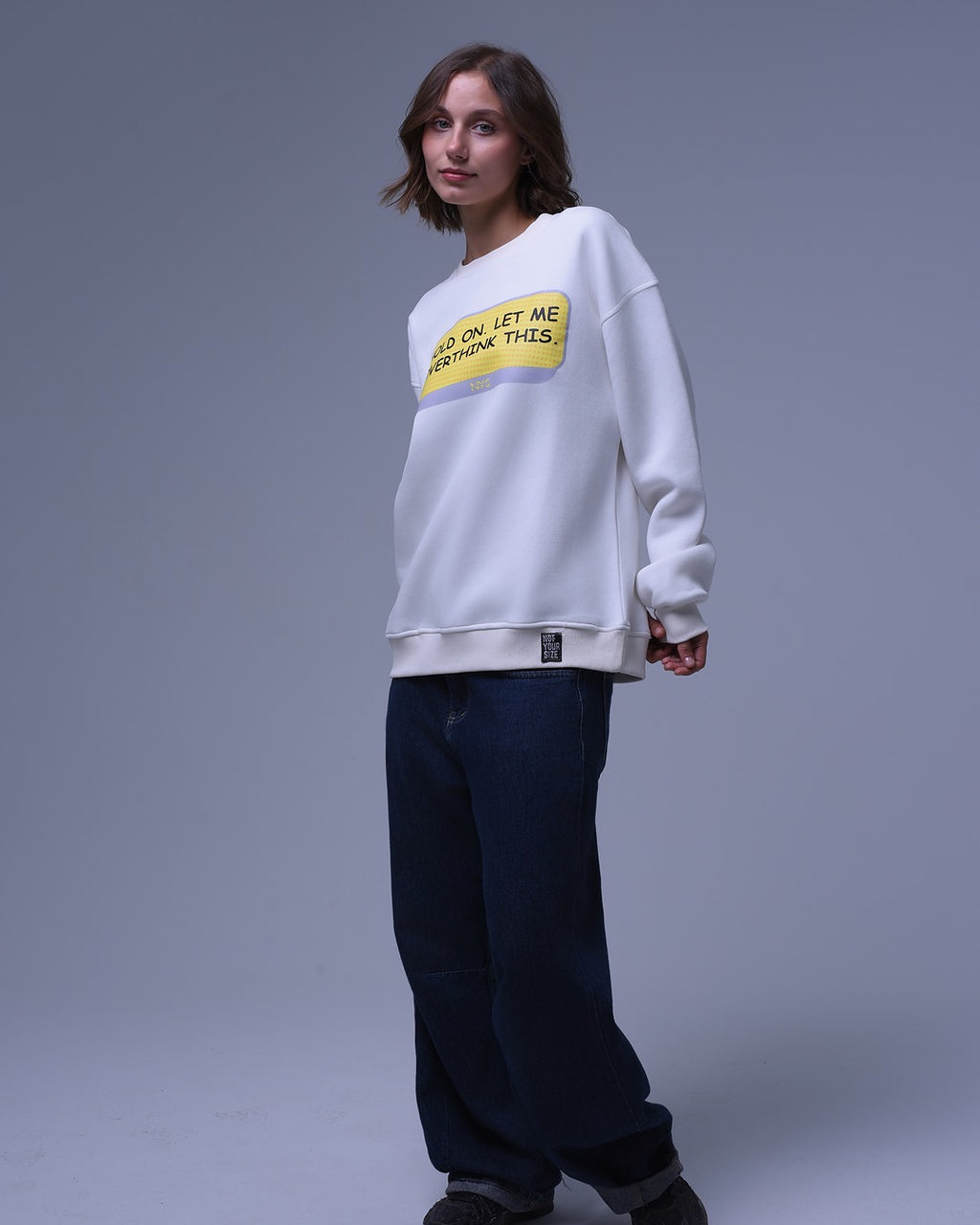 NotYourSize2025 oversized crewneck sweatshirt in white with yellow graphic worn by model with dark pants