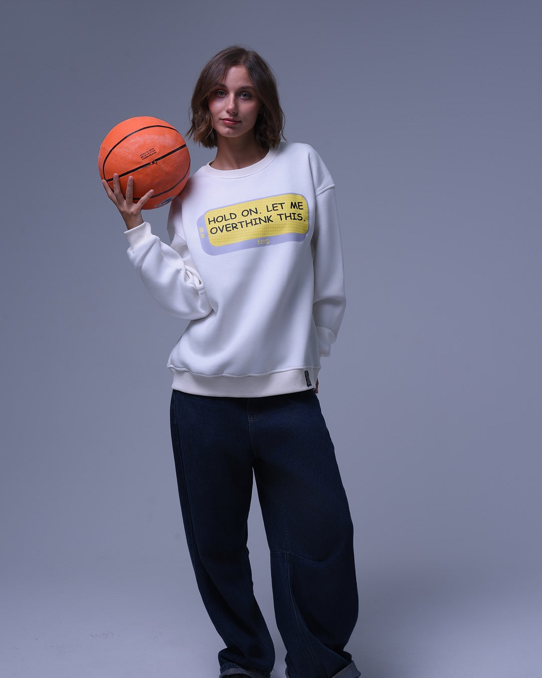 Woman wearing NotYourSize2025 oversized crewneck sweatshirt holding a basketball with printed text design